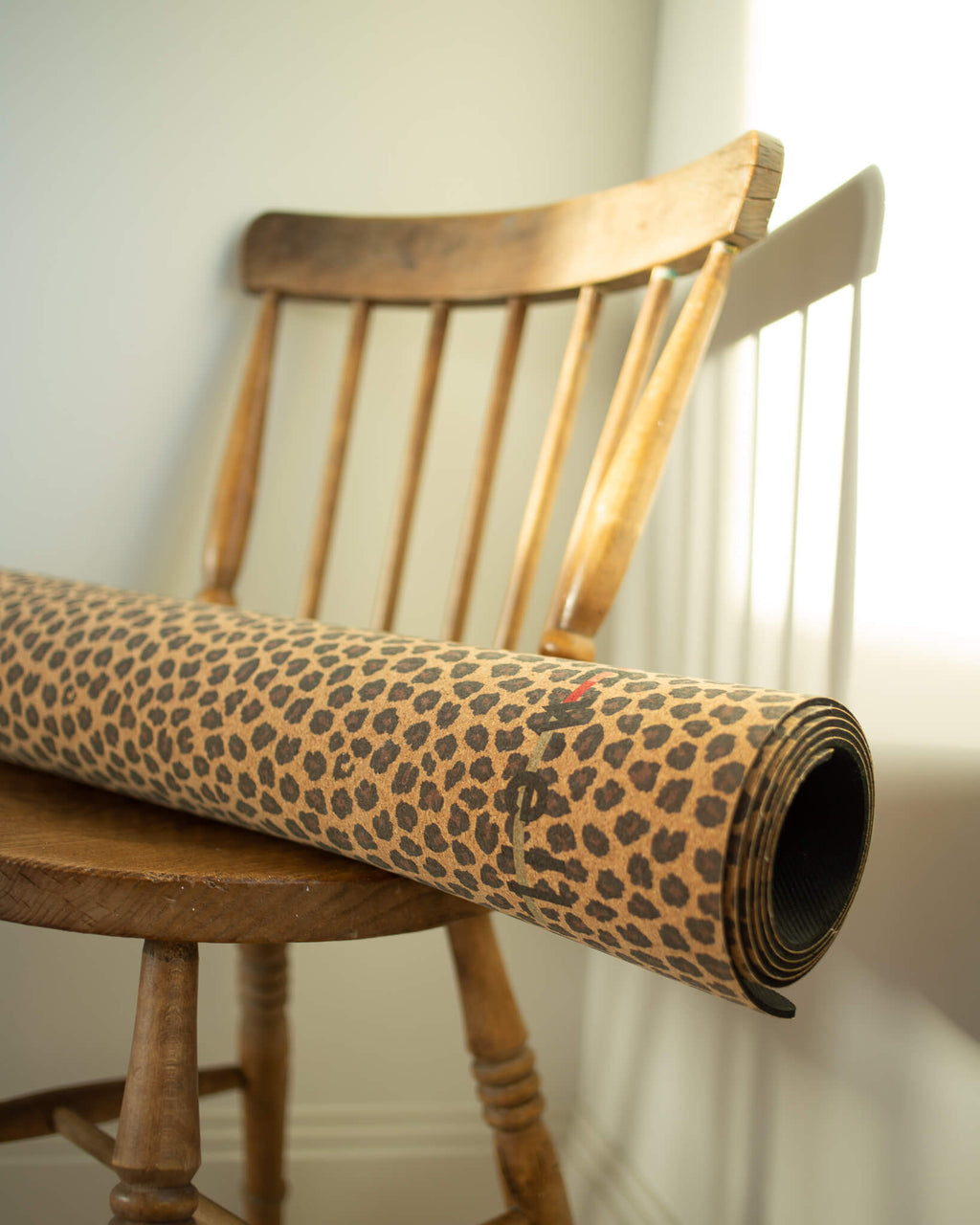 Roll of leopard print paper on a wooden chair against a white wall